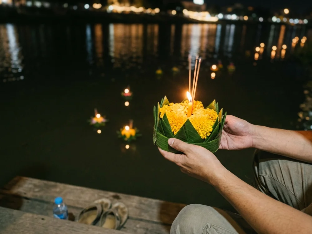 A krathong float held at the edge of the Ping River at night